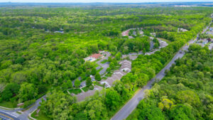 Aerial Exterior, parking lot, view of street, dense woods behind residential buildings.