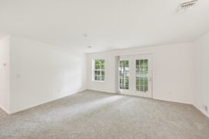 Interior Unit Living Room, white walls, neutral toned carpeting, Window left of patio doors.