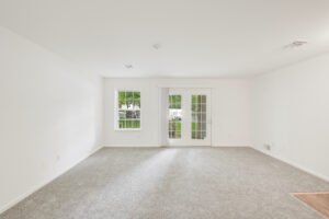 Interior Unit Living Room, white walls, neutral toned carpeting, Window left of patio doors.