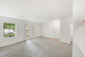 Interior Unit living room, patio doors, white walls, neutral toned carpeting, breakfast bar attached to kitchen.