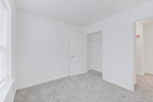 Interior Unit Bedroom, White walls, neutral toned carpeting, closet door.