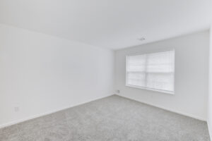 Interior Unit Bedroom, Large window, white walls, neutral toned carpeting.