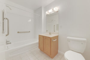 Interior Unit Bathroom, tile flooring, white appliances, light brown cabinetry, vanity mirror, shower/bathtub, white walls.